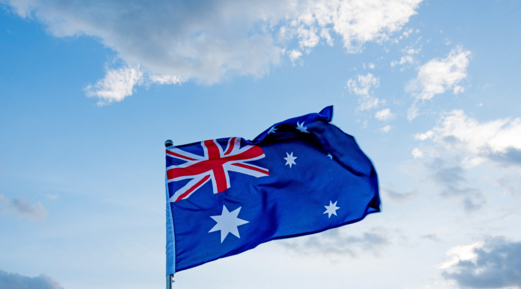 Bandera de Australia ondeando bajo un cielo azul con nubes.