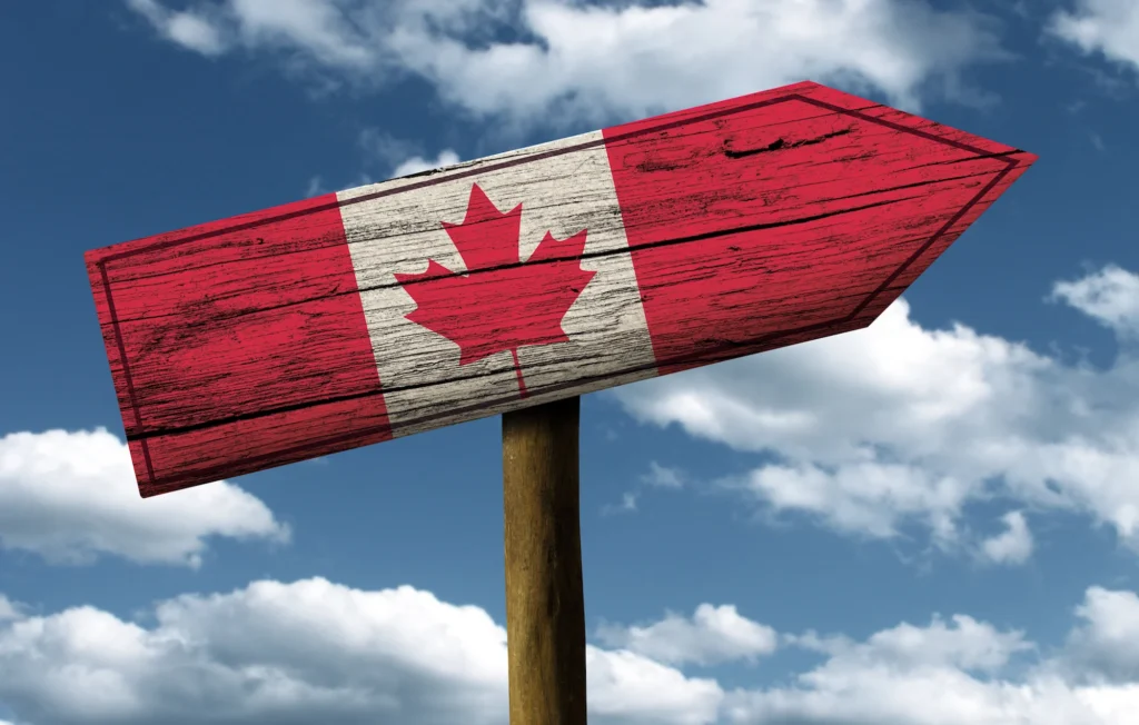 Señal de madera con bandera de Canadá, cielo azul.
